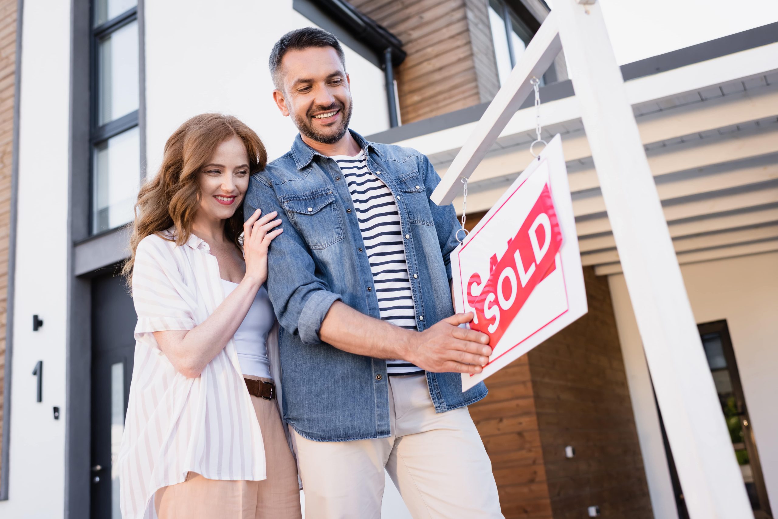 Cheerful couple looking at sign with sold lettering near house